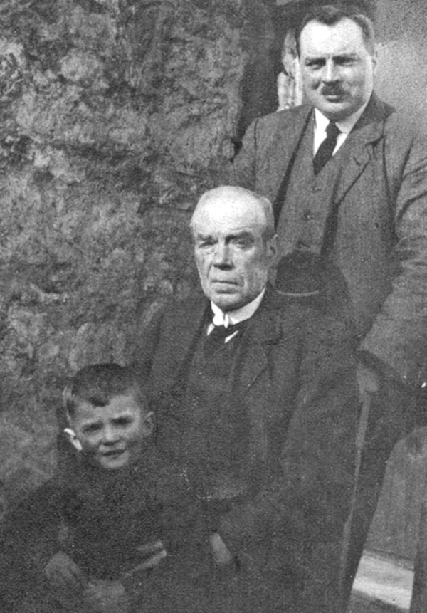 small boy on lap of old man sitting in front of standing man