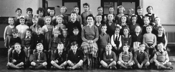 young children sitting alongside and standing behind their class teacher