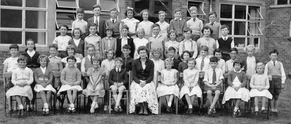 young children sitting alongside and standing behind their class teacher